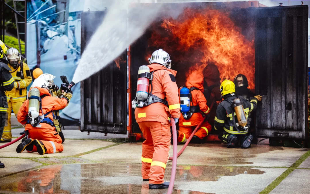 Firefighters in full gear actively extinguishing a blaze during a live fire training exercise outside a burning container.